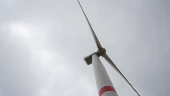 Motion the Blades of a Large Wind Turbine in a Field Against a Background of Cloudy Grey Sky on the