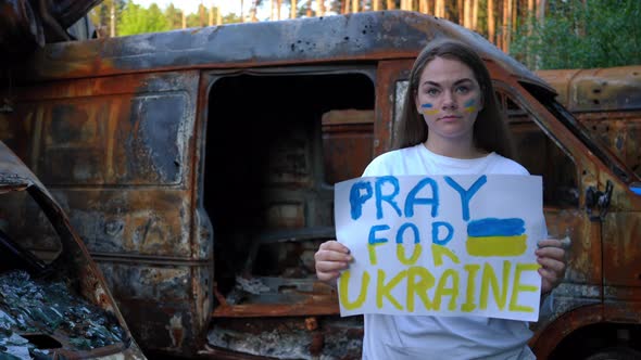 Young Charming Woman with Pray for Ukraine Placard Looking at Camera with Serious Facial Expression