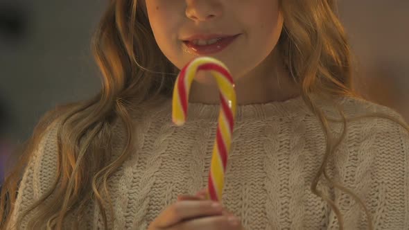 Happy Girl Eating Candy Cane, Enjoying Caramel Sweets at Christmas, Closeup