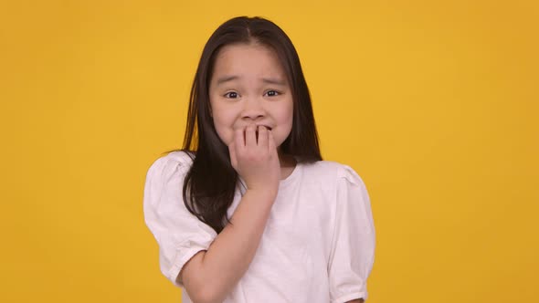 Little Asian Girl Feeling Panic Biting Her Nails Nervously Orange Studio Background Slow Motion