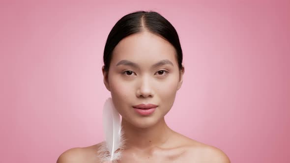 Korean Female Stroking Face With Feather Posing Over Pink Background