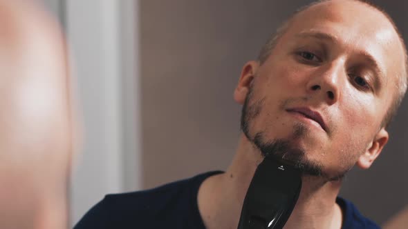 Guy in Black Shaves Beard with Modern Machine in Bathroom