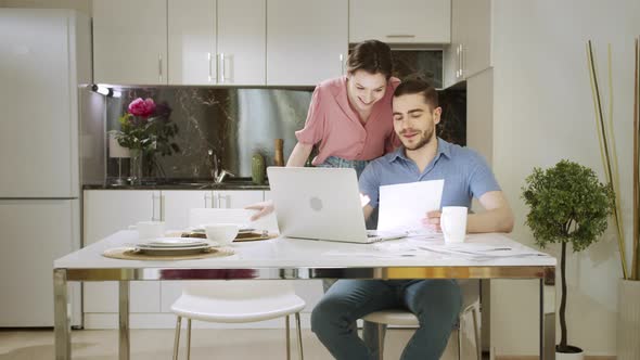 An Adult Man is Sitting and Working at Home and Talking with His Wife