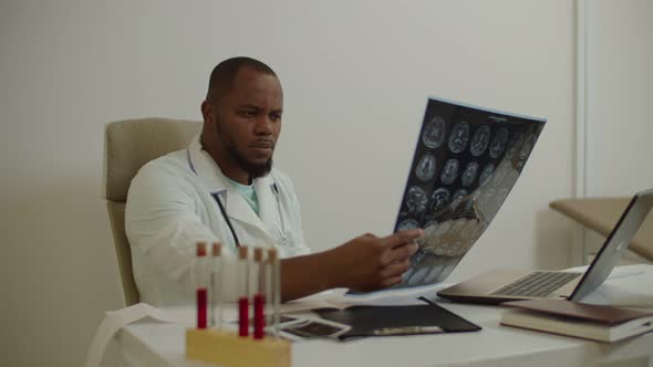 Pensive African American Male Physician Looking at Mri Scan of Ill Patient at Medical Clinic