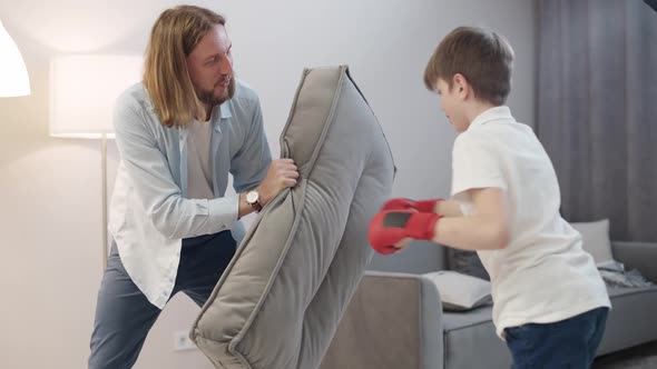 Selfisolation Father and Son Play Boxing a Boy in Red Gloves on His Hands Beats a Sofa Cushion Home