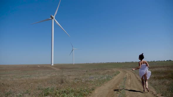 Girl in a White Coat Runs Through a Field with Windmills