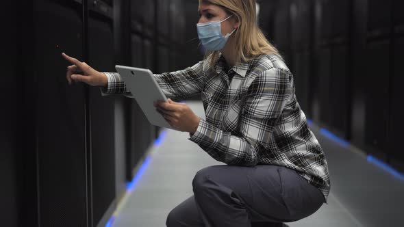 Female informatic engineer working inside server room database while wearing face mask