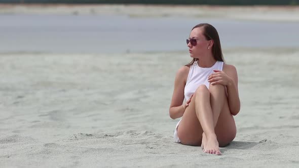 Languid Woman Sitting Cross-legged on Sand Touching Skin