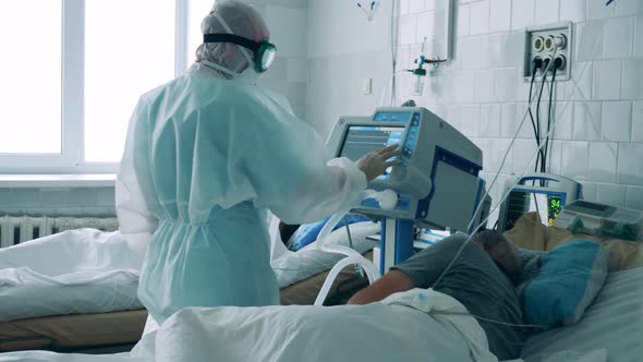 Doctor in a Hazmat Suit Is Operating a Medical Monitor