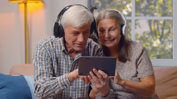 Happy Elderly Man and Woman in Headphones Watching Video on Tablet Pc at Home