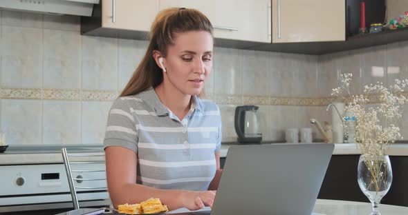 Businesswoman in Wireless Headphones Looks at Laptop Screen