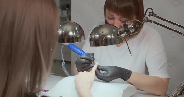 Manicurist Files Client Nails with Machine in Beauty Salon