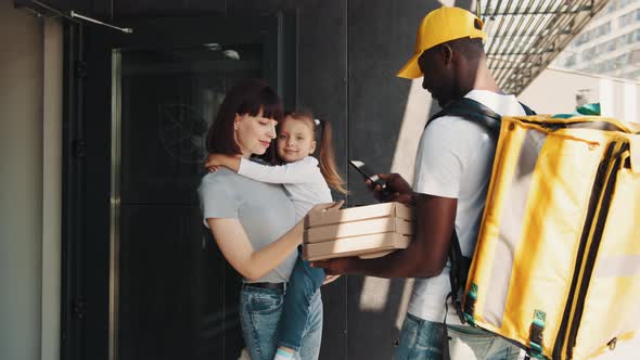 Young Smiling Woman with a Girl at the Door Pay By Card for Online Ordering