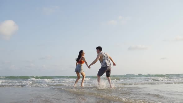 Asian young man and woman having fun, playing on the beach together on holiday vacation.