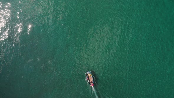 Two boats move at calm clear blue water, top-down aerial (drone) perspective.