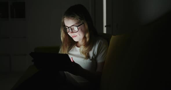 Girl Using Tablet at Home at Night. Pan Left View of Preteen Girl in Glasses Smiling and Browsing