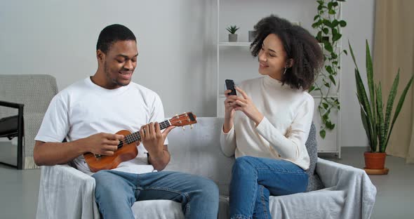 Afroamerican Musician Teacher Artist Plays Small Guitar Sings Looks at Camera of Mobile Phone Curly