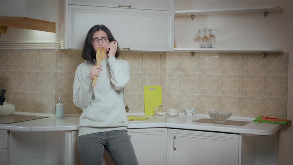 Girl is Having Fun on the Background of the Kitchen at Home Holding a Wooden Spoon and Singing