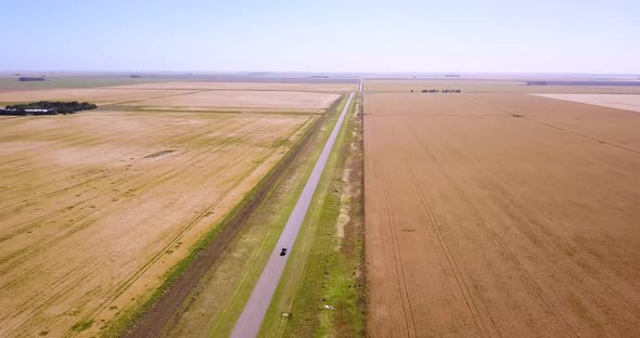 Aerial View Of Vehicle On Country Road Driving Through Farmland At Daytime - drone shot