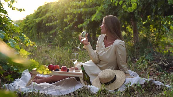 Beautiful Woman with Long Hair Drinks White Wine From a Glass at Sunset in the Vineyard
