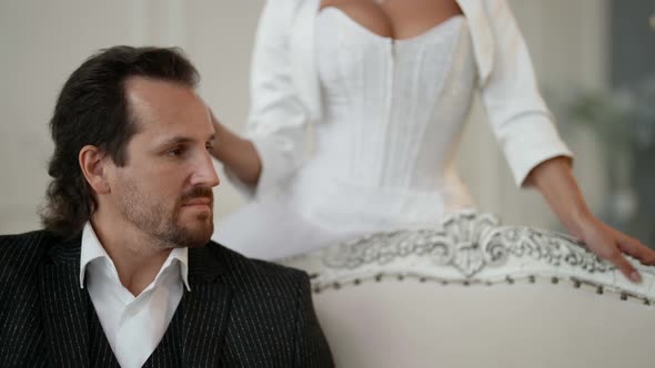 an Unshaven Man in a Suit is Sitting on a Light Sofa