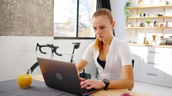 Young Woman is Typing on Laptop Sitting at Table in Kitchen at Home