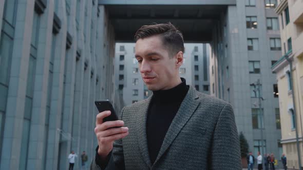 Confident Young Businessman in Official Suit Using His Smartphone App Near Modern Office Building