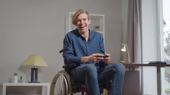 Portrait of Joyful Caucasian Young Handicapped Man in Wheelchair Winning in Multiplayer Online Video