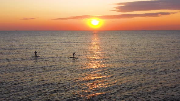 Young woman silhouette on a stand up paddle board. Sunset light in the water.