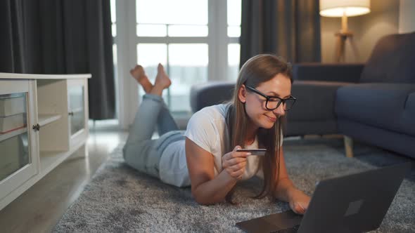 Woman Is Lying on the Floor and Makes an Online Purchase Using a Credit Card and Laptop. Online