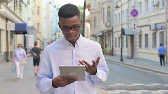 African Man Making Video Call on Tablet While Walking on the Street