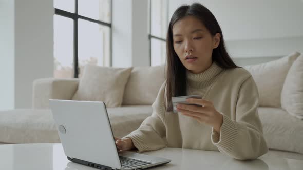 An Asian Woman Shopping Online Using a Laptop While Holding a Credit Card