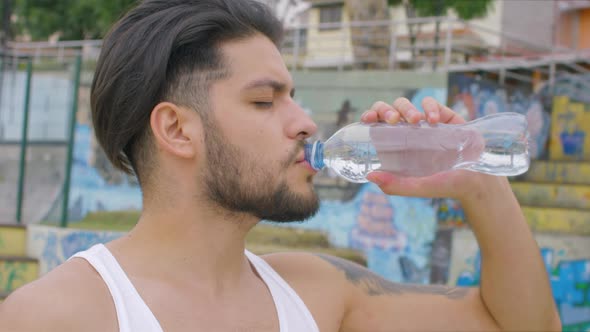 handsome guy drinking fresh water from a plastic bottle in a skate park