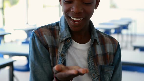 Happy schoolboy looking at hand in classroom