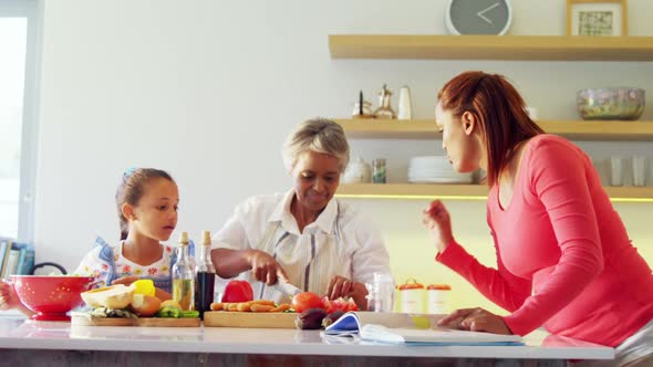 Mother looking recipe book while grandmother and granddaughter chopping vegetables