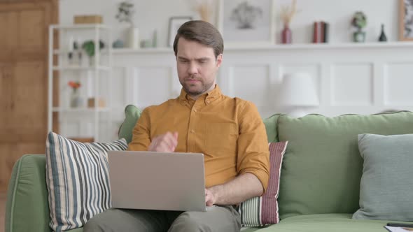 Young Man Thinking while Working on Laptop on Sofa