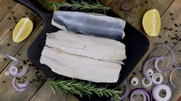 Fillet of Salted Herring with Onions Lemon and Rosemary on Dark Cutting Board Rotating