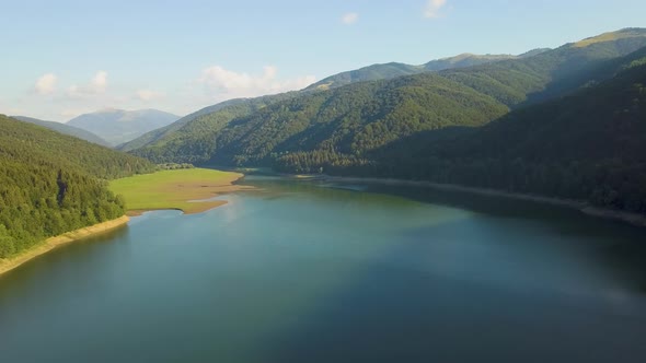 Aerial view of big lake with clear blue water between high mountain hills covered with dense