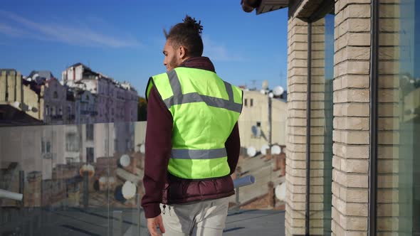 Joyful Confident Builder Walking to Glass Fence on Rooftop Looking at Urban City Down Smiling