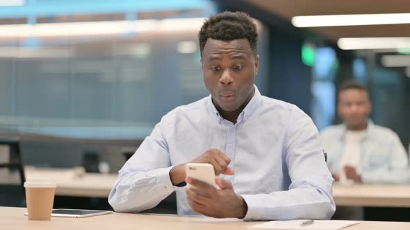 African Businessman Celebrating Success on Smartphone in Office