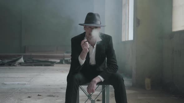 Mature Man Siting in the Chair in the Destoyed Dirty Place with a Fedora Hat and a Classical Suit