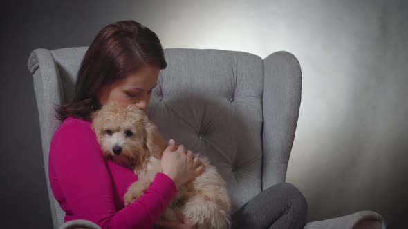 Beautiful Woman Is Playing with a Small Puppy on Chair