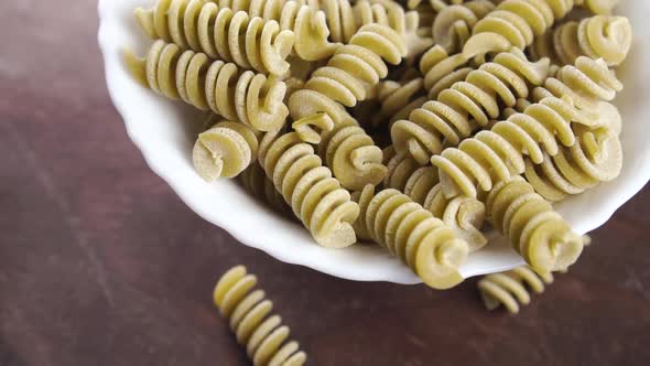 Uncooked pea fusilli pasta. Full bowl of green italian spiral vegetable macaroni on a wooden surface