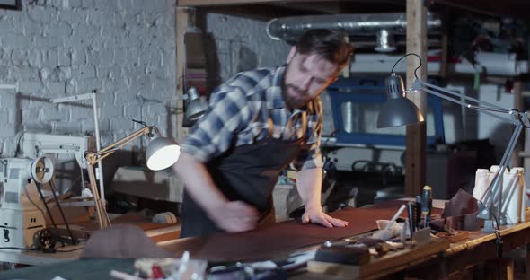 Male Artisan Rolling Leather in Workshop