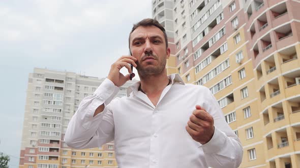 A Businessman in a White Shirt Speaks Emotionally on the Phone