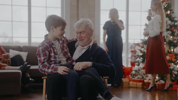 Boy Sits on a Chair with His Grandad and Talks at Christmas Celebration