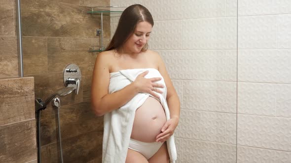 Happy Smiling Pregnant Woman Stroking and Touching Her Growing Belly in Bathroom