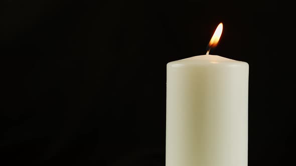 A Burning White Candle on a Black Background or in the Dark