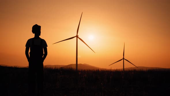 Silhouette Man Standing on Field with Huge Windmills During Summer Sunset