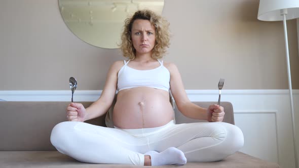 Hungry Dissatisfied Pregnant Woman Holding Spoon And Fork In Hands Waiting For Food